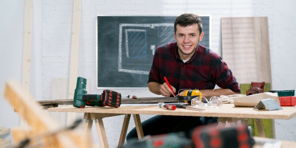 Close-up of a hardworking professional carpenter holding a angular ruler and pencil while measuring a board in a carpentry workshop