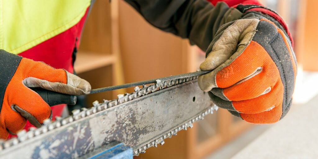 Close up on a man sharpening a chainsaw chain with file.