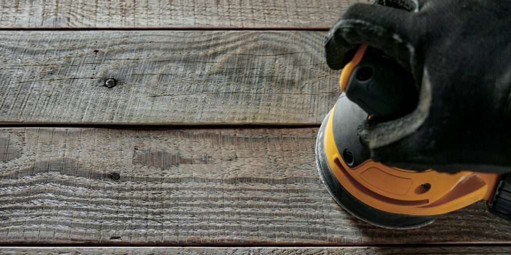 Top view of hand holding orbital sander on wooden boards.